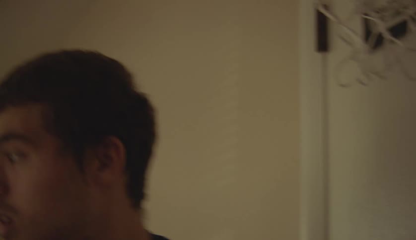 A teenage boy hangs a small basketball hoop on the back of a door and walks away