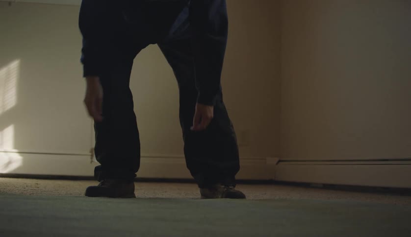 Man with black pants and sweater lays rug on floor in room