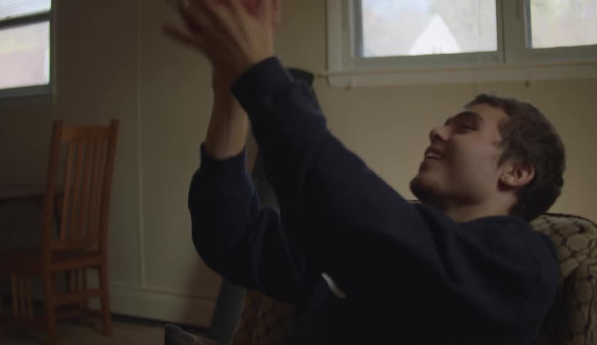 Man in dark blue sweater sits in brown armchair and shoots toy basketball in room