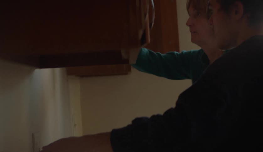 Middle aged woman with light blue sweater turns on lights next to man in the kitchen