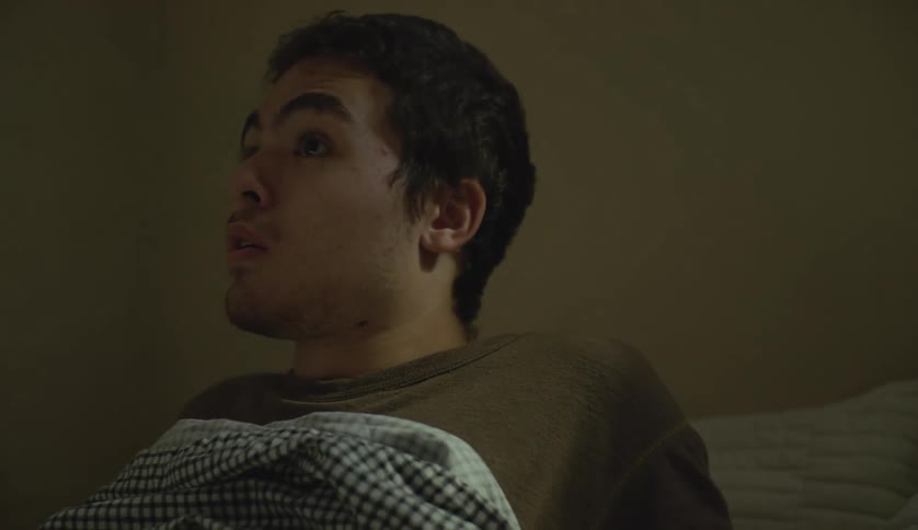 A young white man is laying down in his bedroom