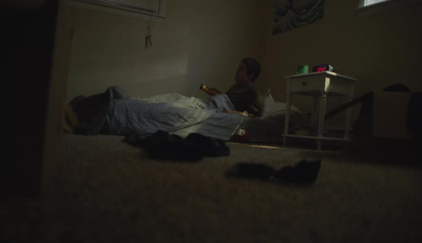 A young white man is laying down inside of his room