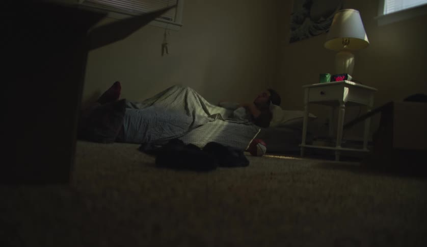 Young man goes to sleep over a mattress on the floor of a dimly lit room