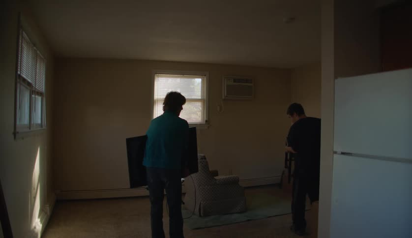 Two people are moving furniture inside of a house