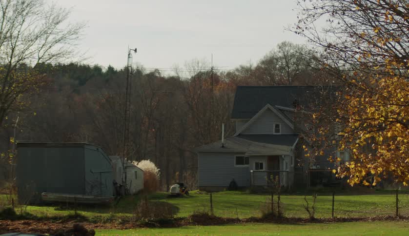 Remaining leaves on trees near farmhouse flutter in breeze