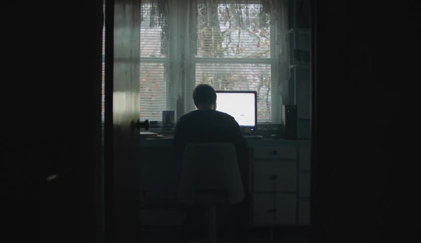 There is a white man that is inside and is on his laptop