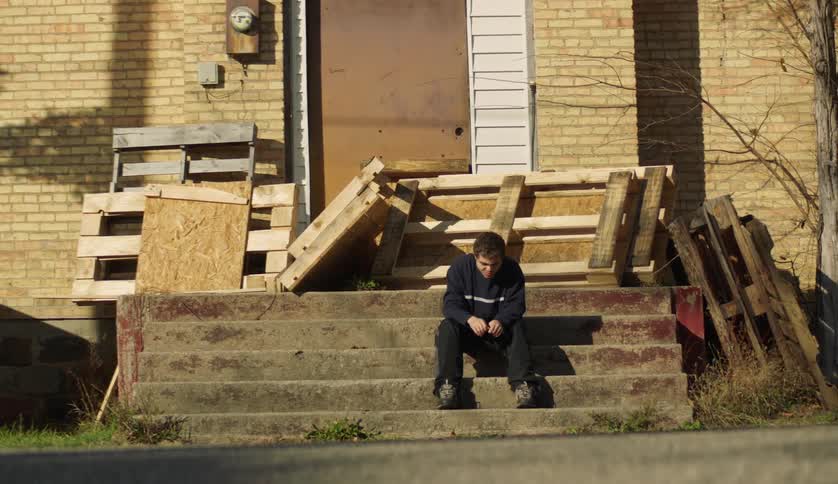 A young white man is sitting on some stairs outside
