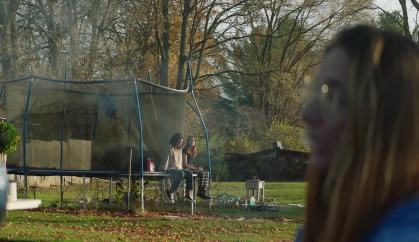 A woman is smoking as teenagers sit on the trampoline