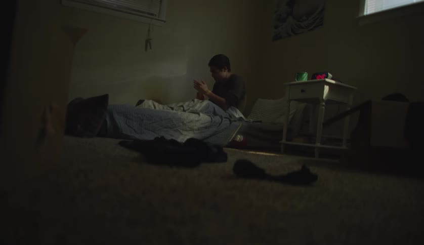 A young man is laying down on his bed in his room