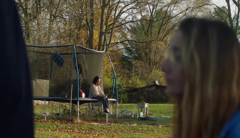 Man walks away after talking to woman before turning backas others sit and walk on trampoline in background