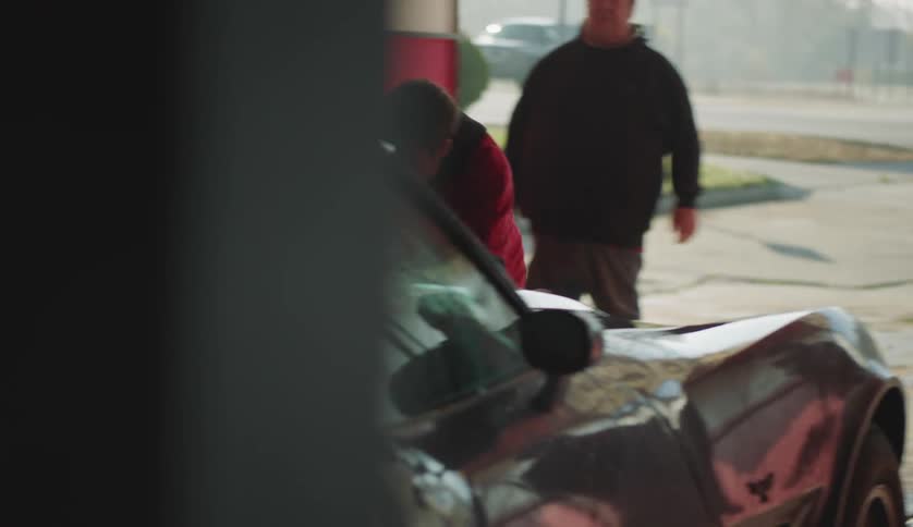 Man dries car at car wash while coworkers and driver watch