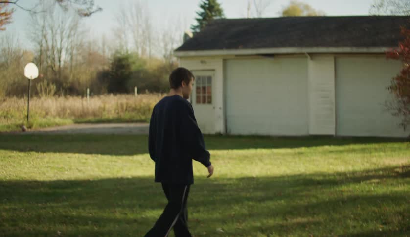 Man with dark blue sweater walks on green lawn in the front yard of the house