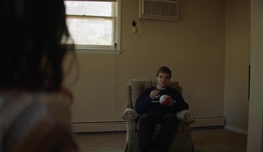 A teenage boy is sitting in a chair playing with a ball as he turns around and talks to his friend