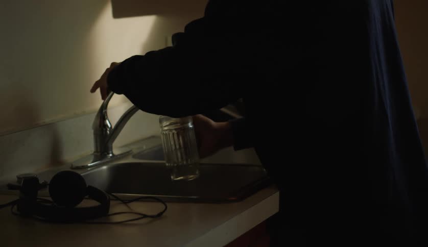 Man with dark blue sweater fills glass with water in the kitchen