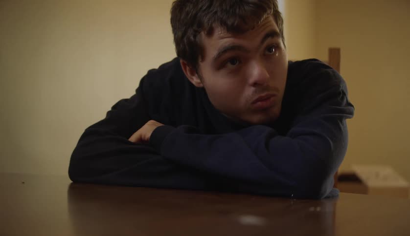 A male is sitting at a table in his house
