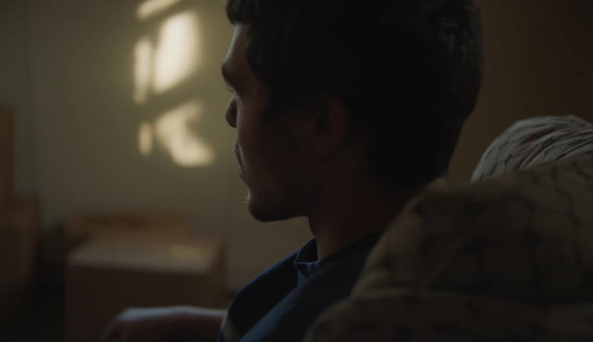 Man in dark blue t shirt sits in armchair in room with boxes
