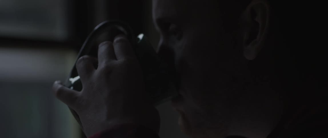 A man drinks from a mug in a dark room