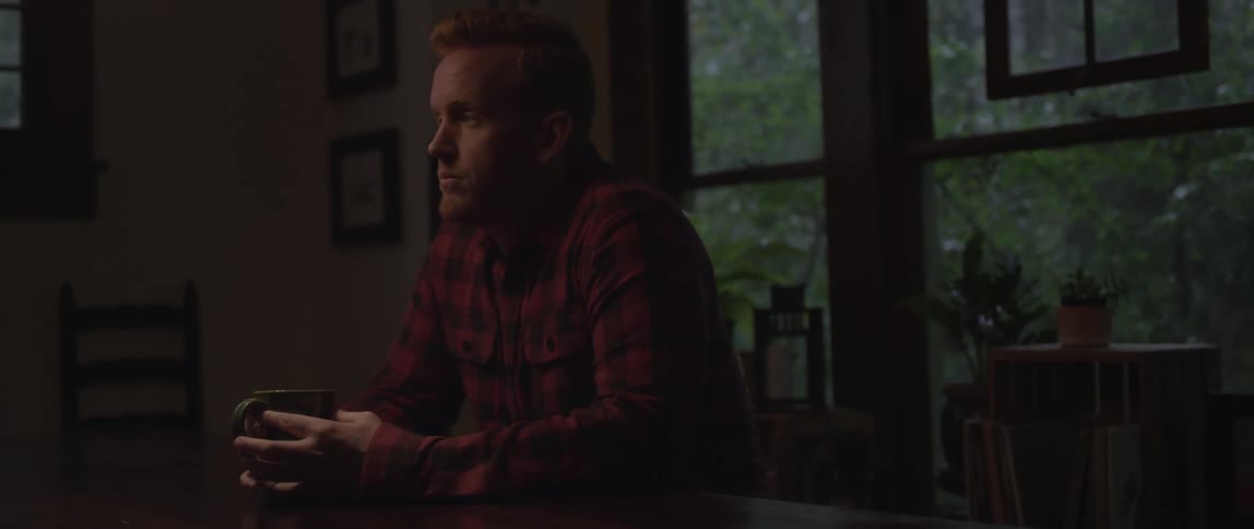 A man is sitting in his home holding a mug