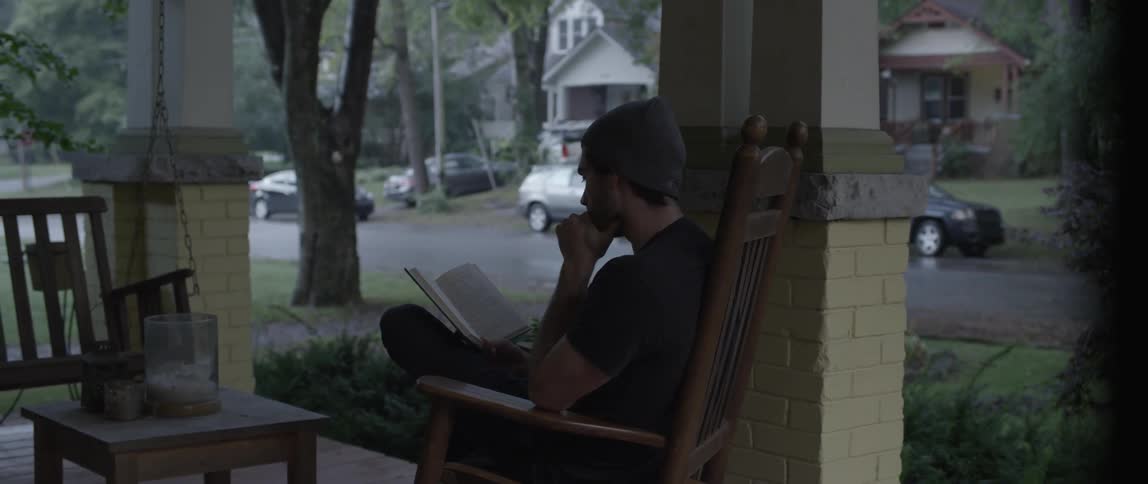 A man sits on his porch reading a book