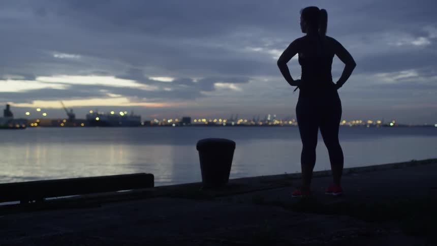 A woman stands by the water at sunset