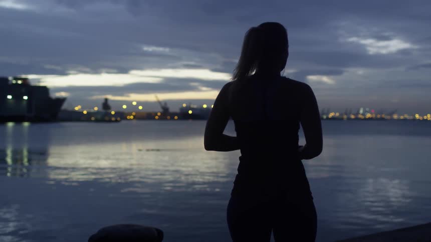 A woman walks towards the water at sunset