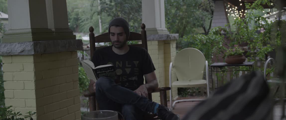 A man sits on a porch reading a book