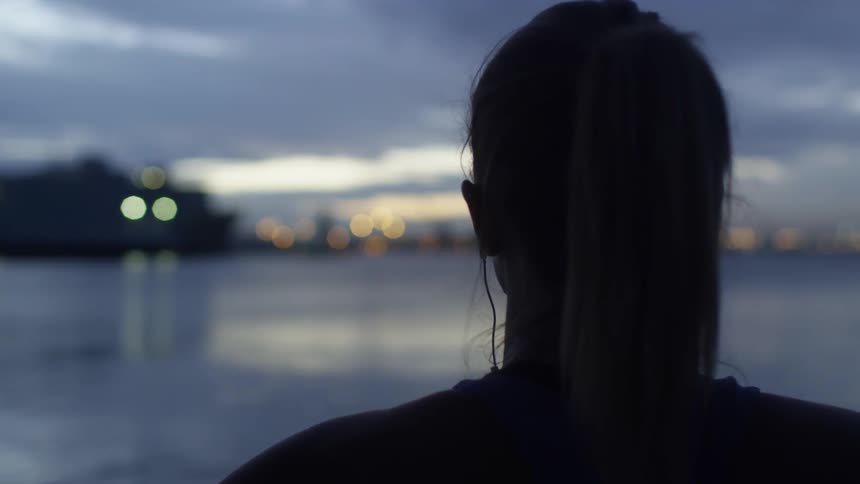 A woman is looking out over the water at sunset