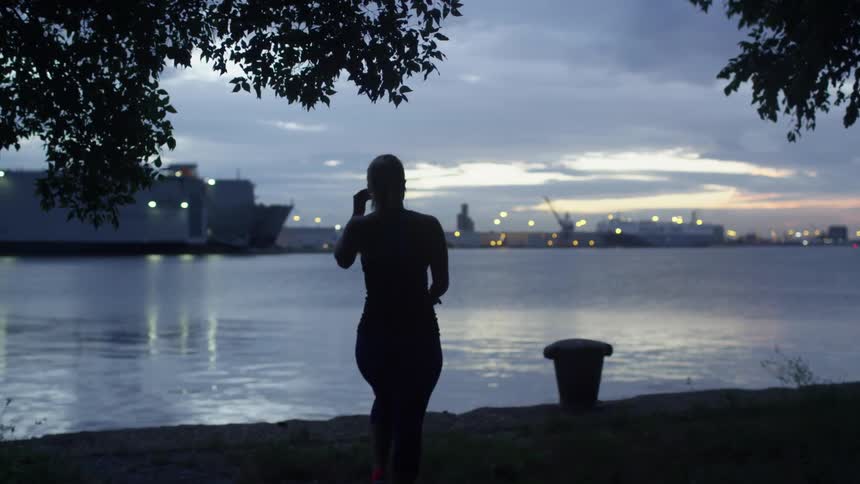 A woman walks toward the river at dusk