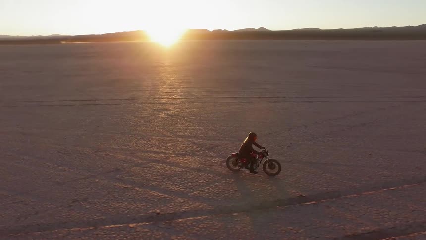 A person is racing a motorcycle over the desert at sunset