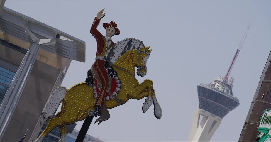 Business sign in shape of horseman and horse sits above american flag near buildings with space needle in the background