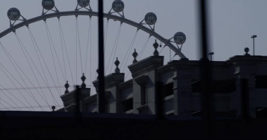 An area of a city is being filmed left to right revealing a ferris wheel a sign a building and traffic lights