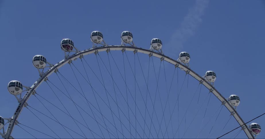 The sun shines on a ferris wheel as it turns high in the blue sky