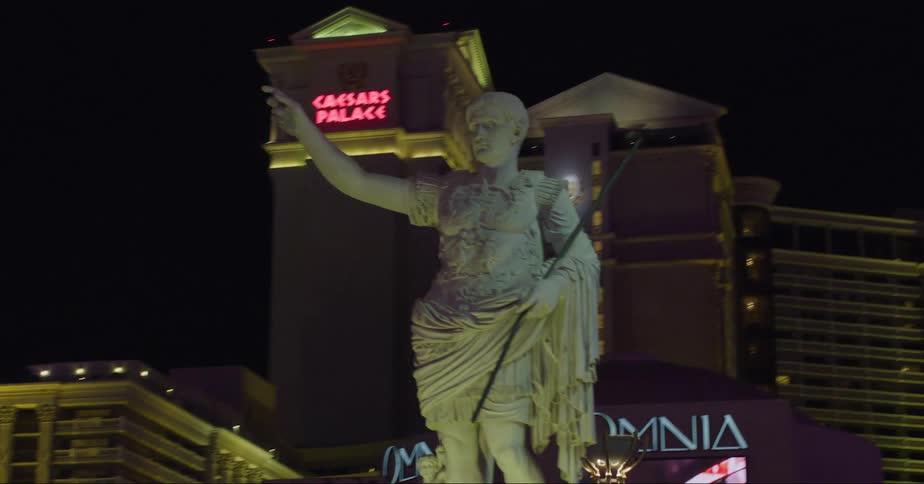 A statue in front of lit up hotels at night