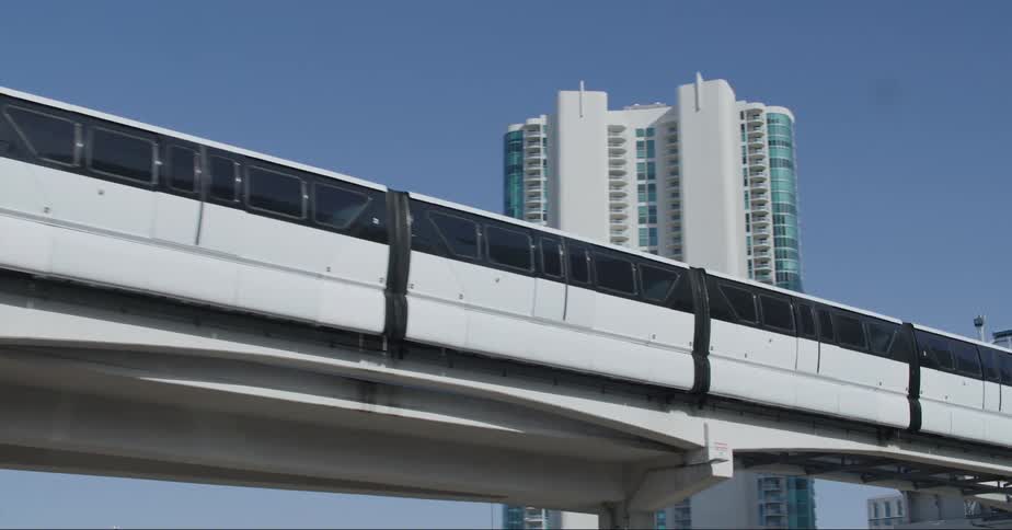 Train sits parked on elevated track near terminal above busy freeway near skyscrapers