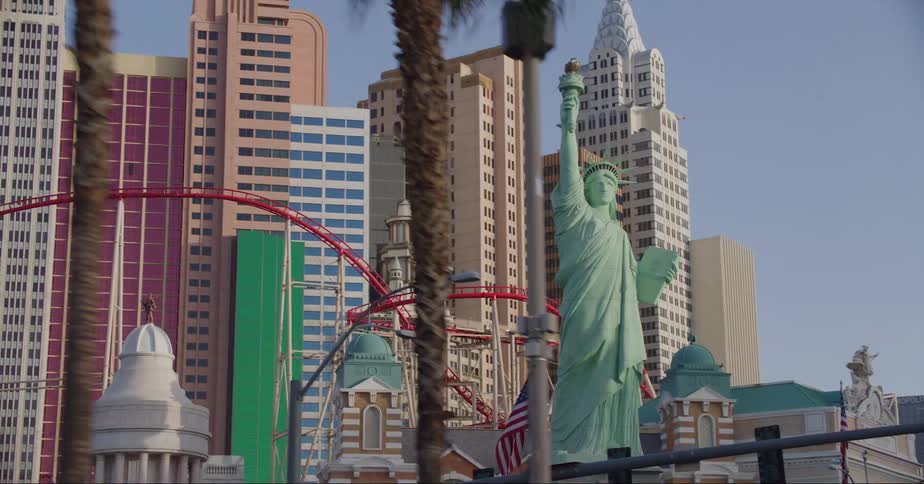 A rollercoaster and a statue of liberty in front of tall buildings at an amusement park