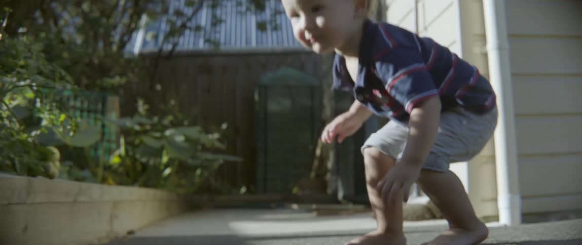 Young toddler boy playing with a curious domestic cat on a sunny outdoor patio.