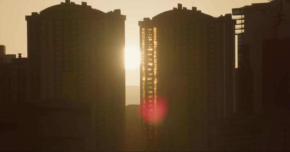 Sunset sun shines between the silhouette of buildings in the city skyline
