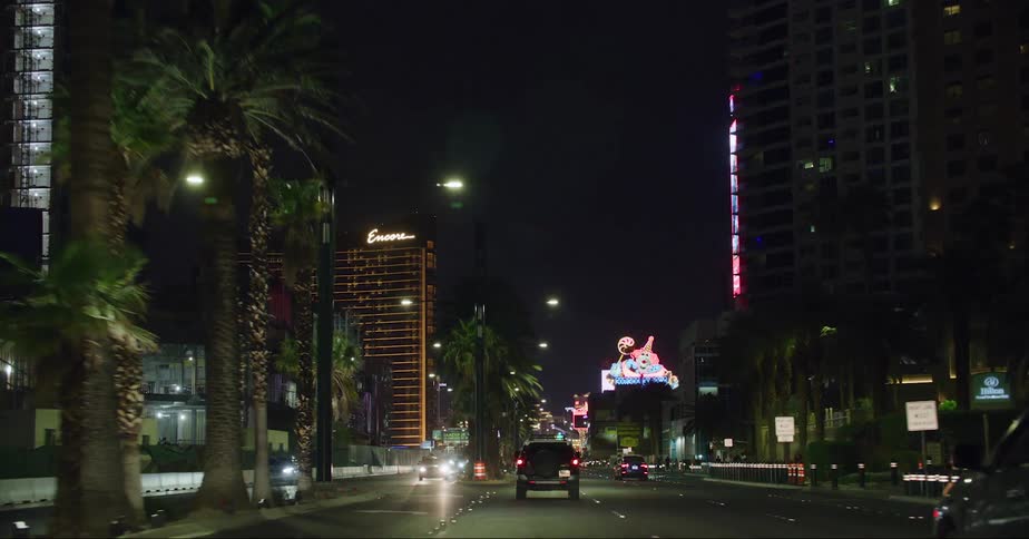 Traffic moves along street passing buildings and casinos with neon signage on las vegas strip at night