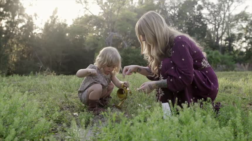 A woman helps a child water some grass