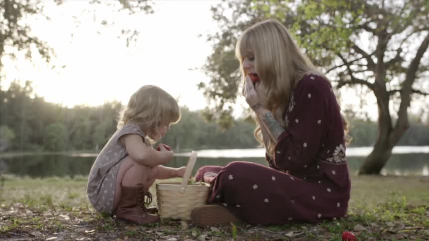 A woman and child eat fruit near a lake