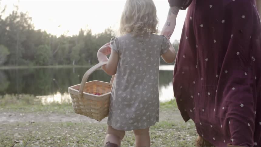 A woman and child holding a basket walk towards a lake