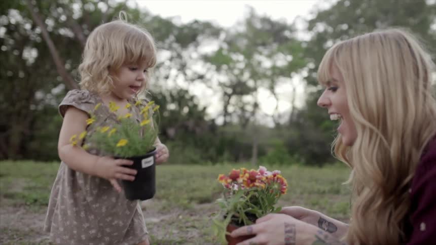 A woman crouches down to a child to compare pots of flowers