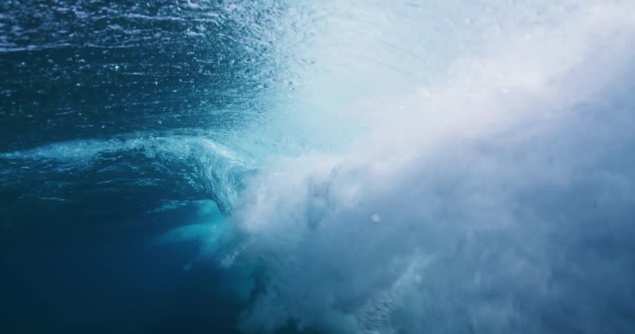 Underwater view of a wave rolling overhead and sunlight reflecting the ripples as water splashes