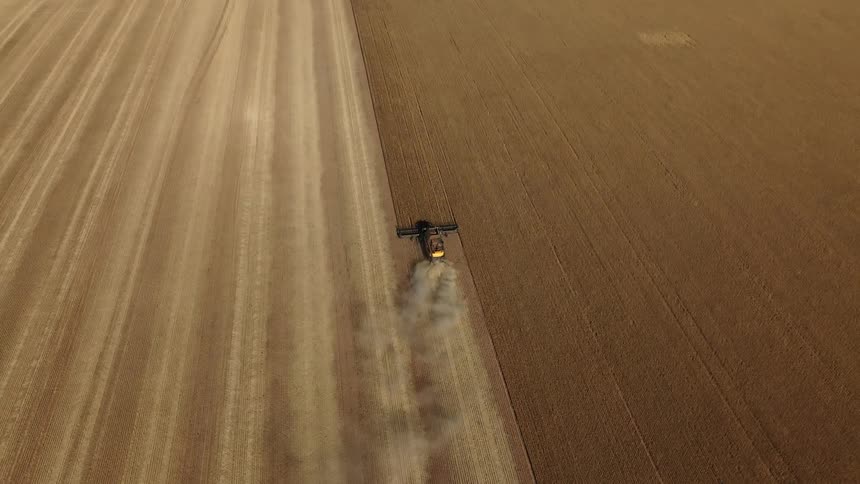 A tractor is plowing a field on a farm and leaving behind a cloud of smoke