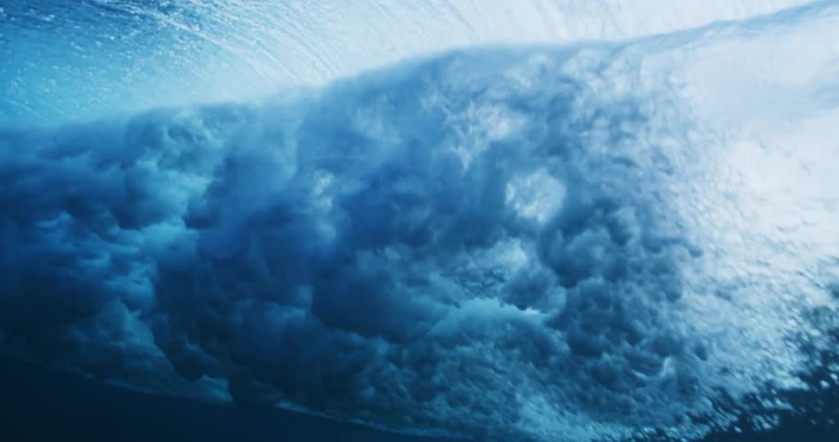 Underwater view of a wave rolling overhead and sunlight reflecting the ripples and sparkles as water splashes