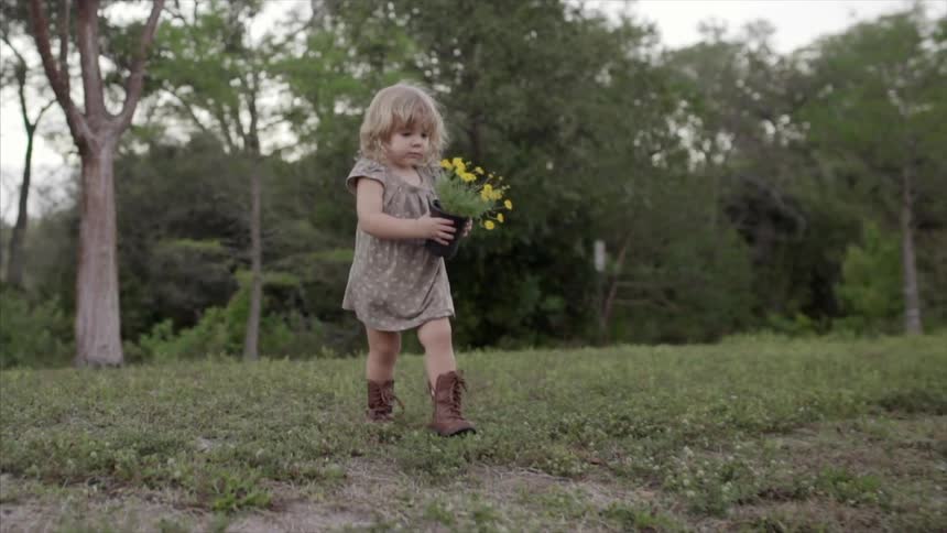 A little girl crossing a field as she carries a pot of yellow flowers