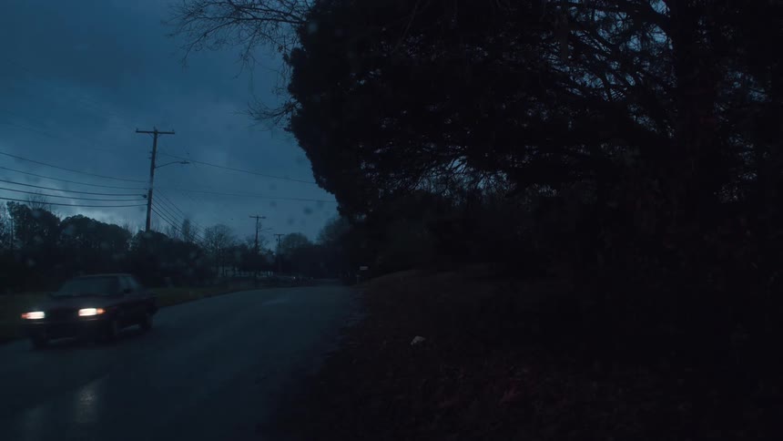 An automobile is traveling on a road in the evening under a cloudy sky