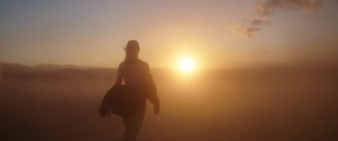 A woman walks through dust clouds on the windy landscape
