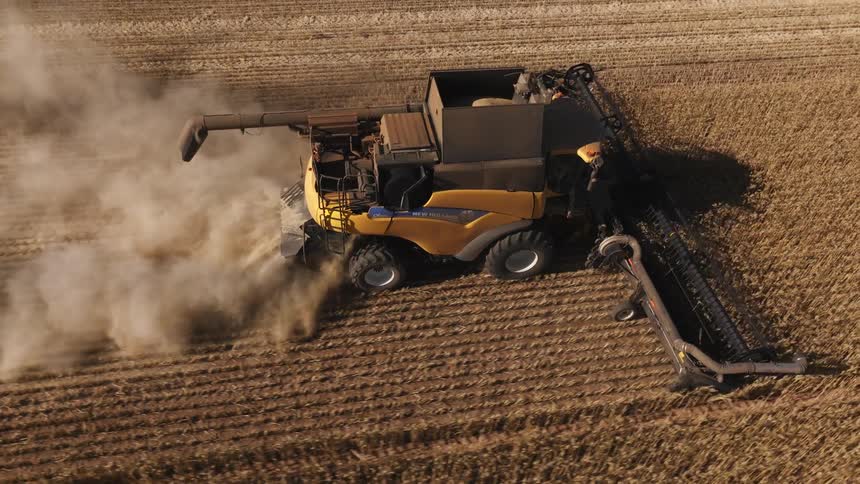 A tractor is plowing a field on a farm and leaving behind a cloud of smoke