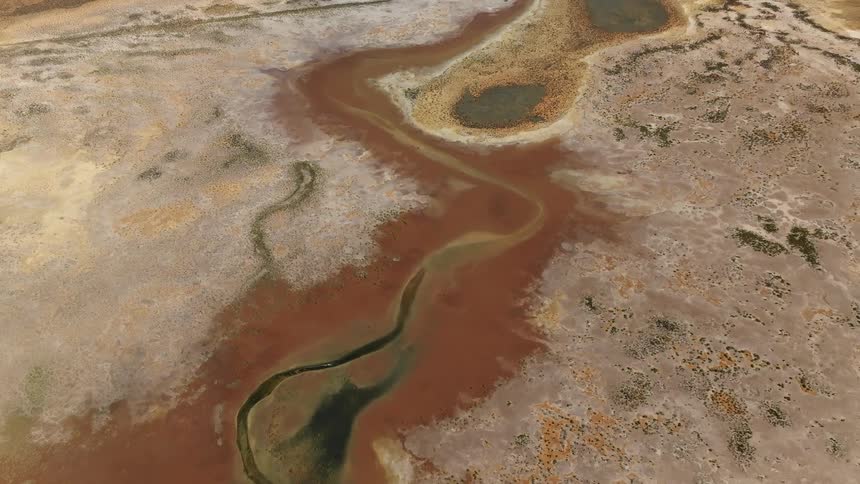 An aerial view of a river flowing through a barren dirt covered terrain